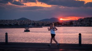 A woman jogs along a waterfront at sunset with a boat in the background.